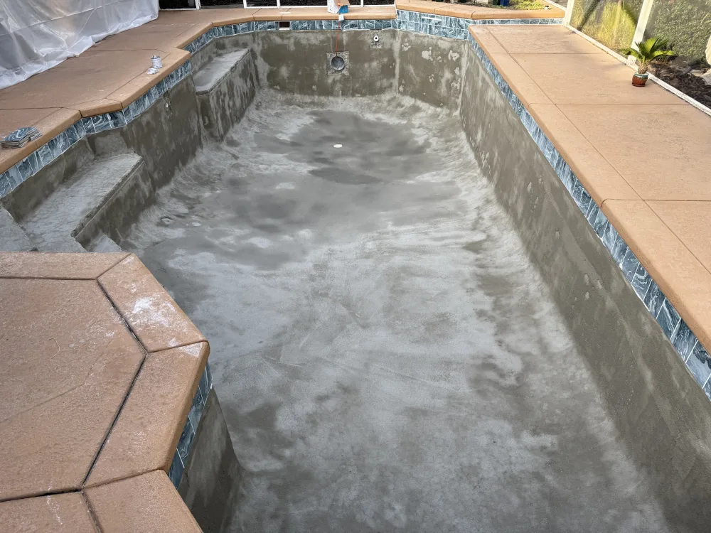 Empty swimming pool under renovation by Kristi's Pool Service, showcasing new concrete surface and tile work.