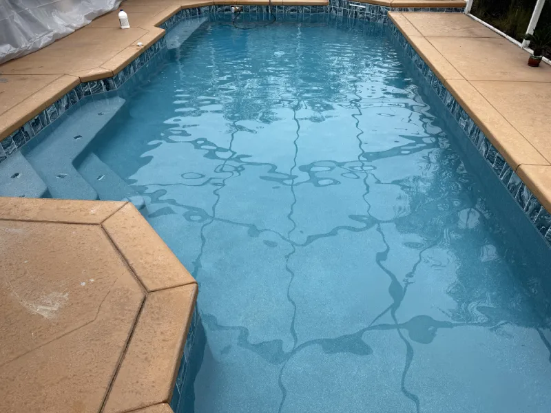 Clean residential swimming pool with clear blue water, serviced by Kristi's Pool Service, featuring tiled edges and steps.