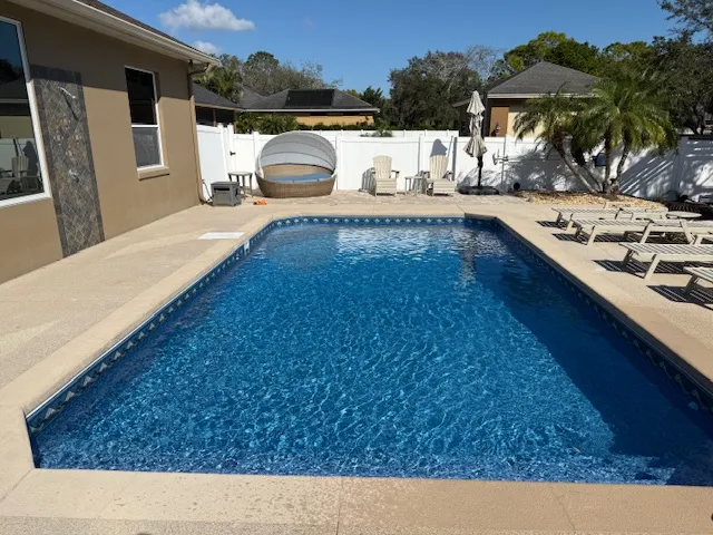 Residential swimming pool with clear blue water, surrounded by lounge chairs and palm trees, serviced by Kristi's Pool Ser...