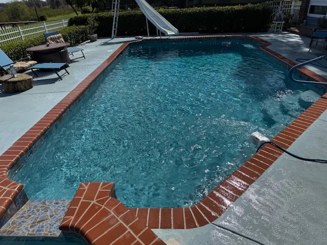 Backyard pool with slide, surrounded by lounge chairs and greenery, serviced by Kristi's Pool Service for clean, clear water.