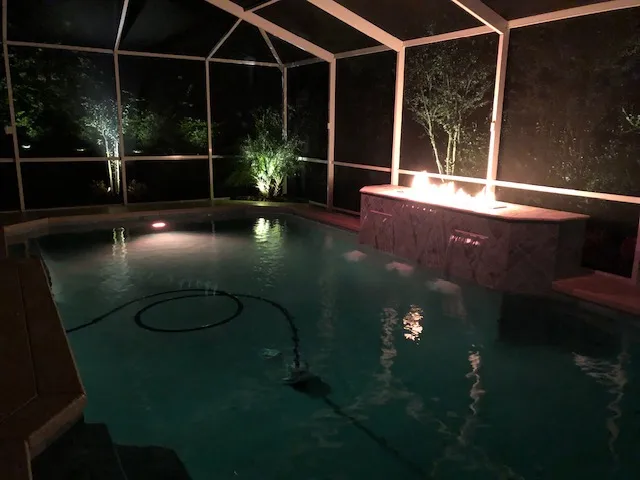 Illuminated pool with cascading waterfalls and ambient lighting, showcasing Kristi's Pool Service's elegant nighttime design.